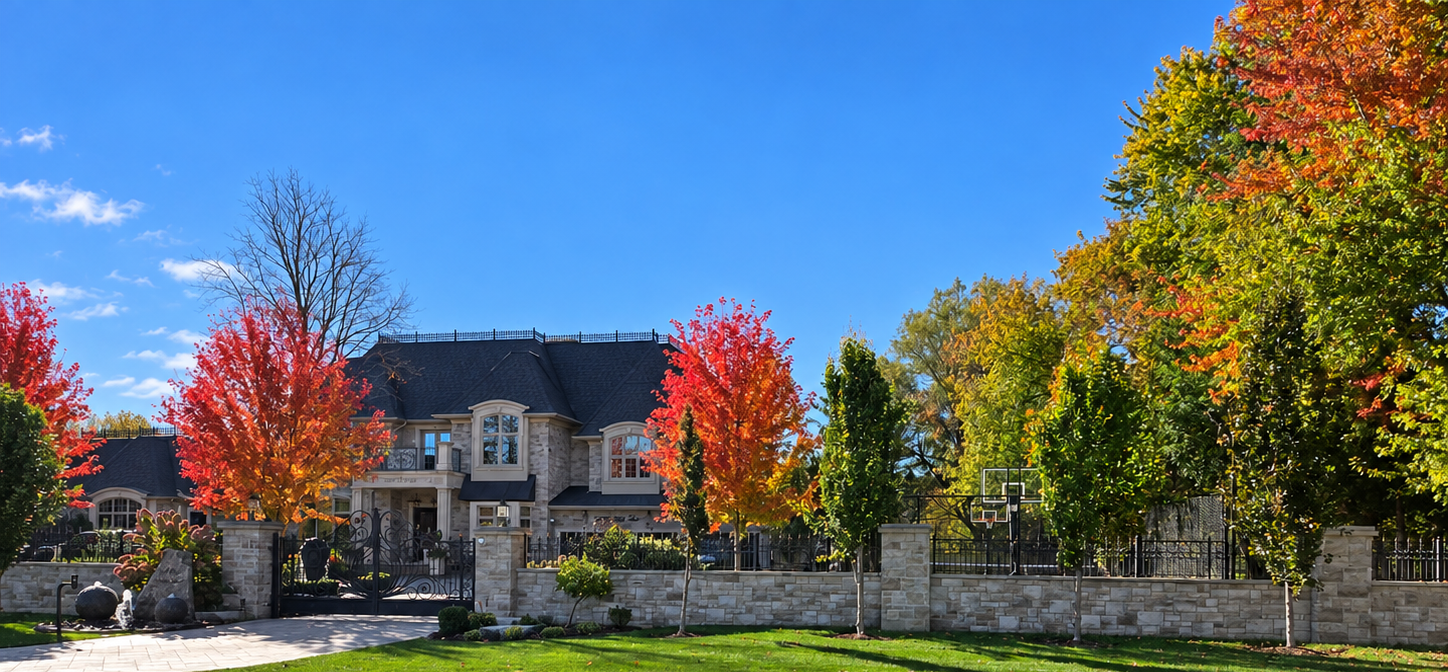 Large stone home behind a landscaped wall with autumn trees
