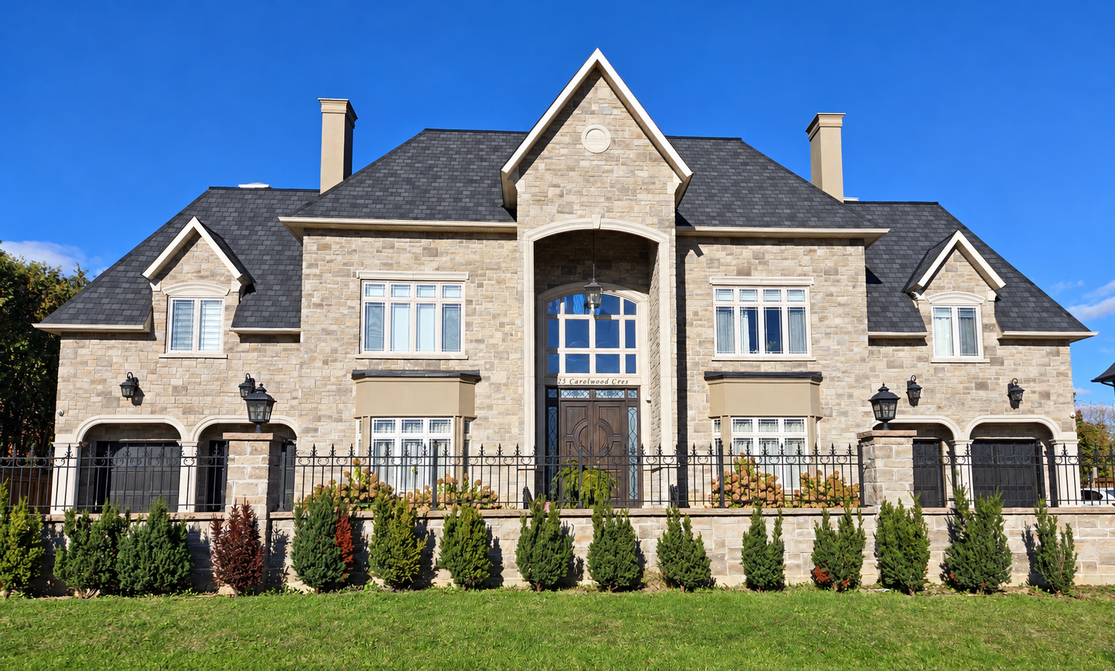 Symmetrical stone home with a gabled center entrance and wrought-iron fence
